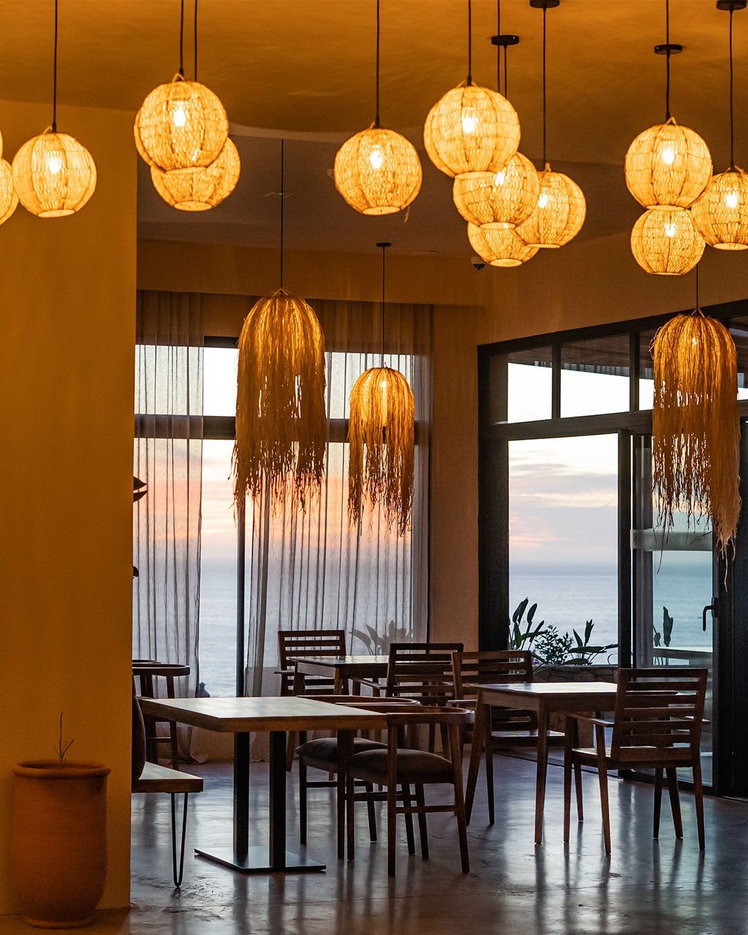 The restaurant at Nobi at dusk, raffia lamps lit and Taghazout Bay through the windows